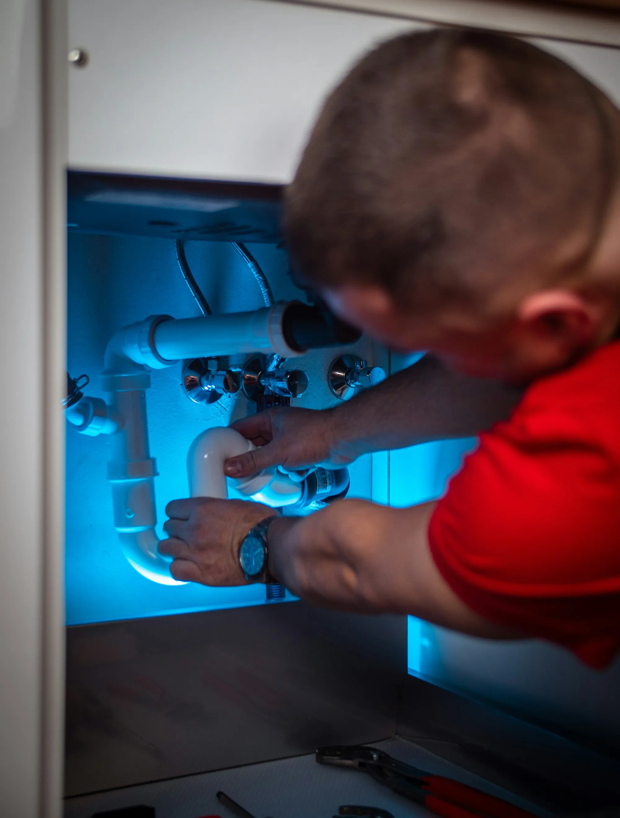 Technician working on a water line inside a sink cabinet